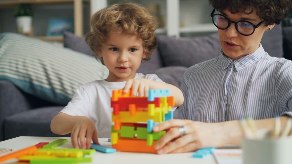 Niño armando una torre de bloques junto a su educadora
